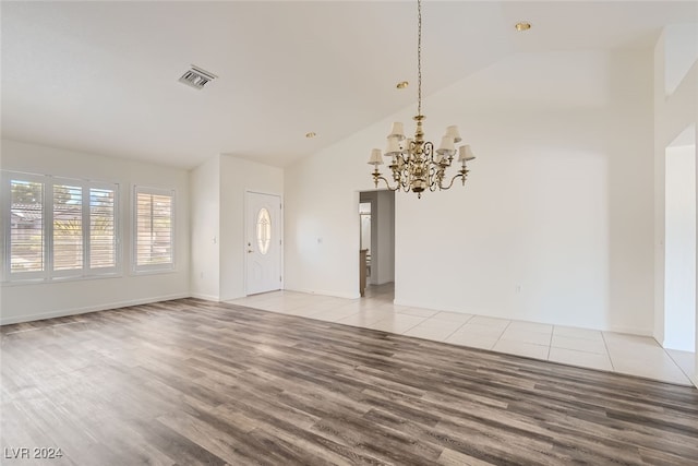 empty room with a chandelier, high vaulted ceiling, and light wood-type flooring