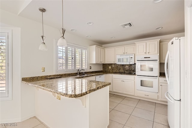 kitchen with white appliances, sink, kitchen peninsula, decorative light fixtures, and dark stone countertops