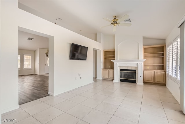 unfurnished living room with ceiling fan, light tile patterned flooring, a fireplace, and built in shelves