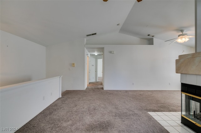 unfurnished living room with a tiled fireplace, lofted ceiling, light colored carpet, and ceiling fan