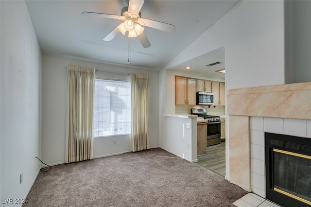 kitchen featuring appliances with stainless steel finishes, lofted ceiling, light carpet, and a tile fireplace