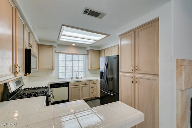 kitchen with tile countertops, gas stove, dishwashing machine, and refrigerator with ice dispenser