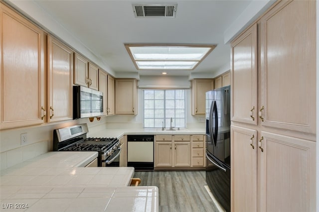 kitchen with tile countertops, appliances with stainless steel finishes, sink, and light brown cabinets