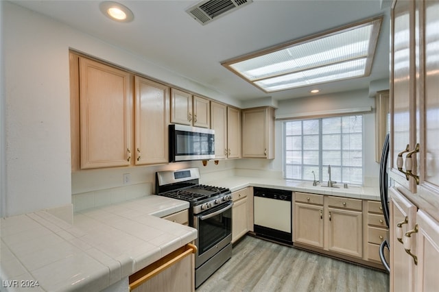 kitchen with appliances with stainless steel finishes, tile counters, light brown cabinets, and light hardwood / wood-style floors