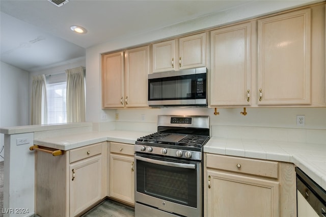 kitchen featuring tile countertops, light brown cabinetry, appliances with stainless steel finishes, and kitchen peninsula