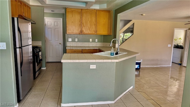 kitchen with sink, kitchen peninsula, stainless steel fridge, black gas range, and light tile patterned floors