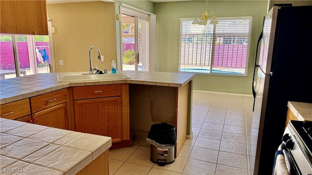 kitchen featuring sink, range, hanging light fixtures, tile counters, and an inviting chandelier