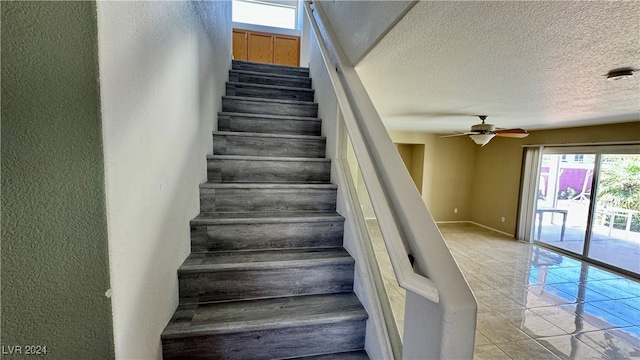 stairway featuring ceiling fan, a textured ceiling, and tile patterned flooring