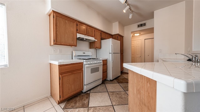 kitchen with white appliances, sink, tile countertops, kitchen peninsula, and rail lighting