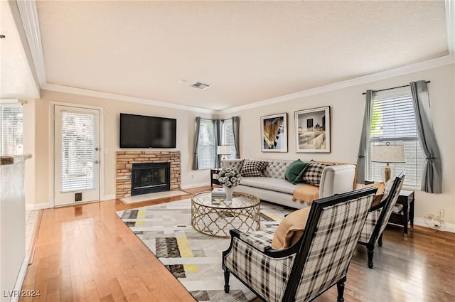 living room featuring wood-type flooring, a stone fireplace, and crown molding