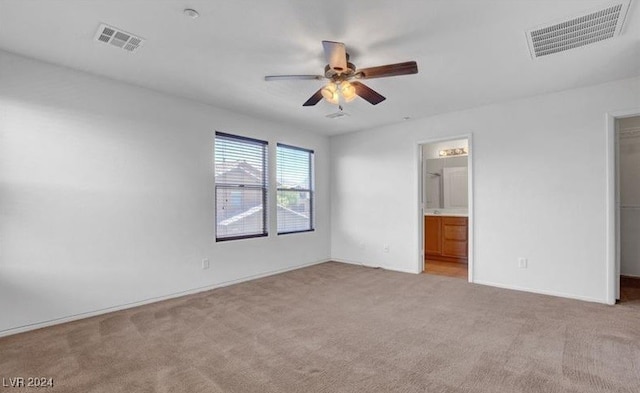 unfurnished bedroom with a walk in closet, ensuite bathroom, light colored carpet, and ceiling fan