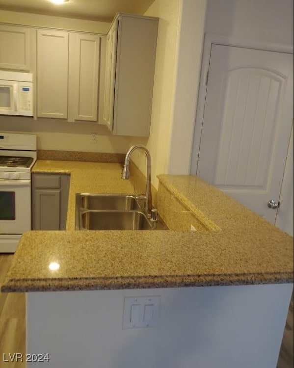 kitchen with sink, wood-type flooring, light stone counters, and white appliances