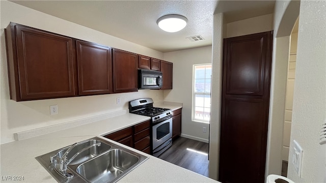 kitchen with dark wood-type flooring, gas stove, a textured ceiling, and sink