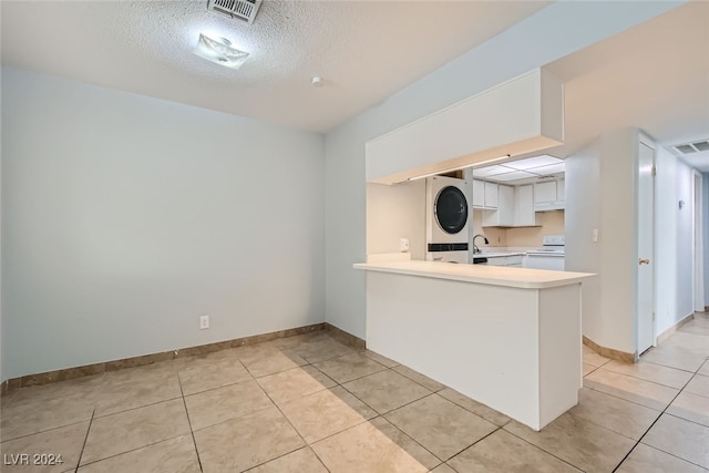 kitchen featuring light tile patterned flooring, kitchen peninsula, stacked washer / drying machine, white range, and white cabinets