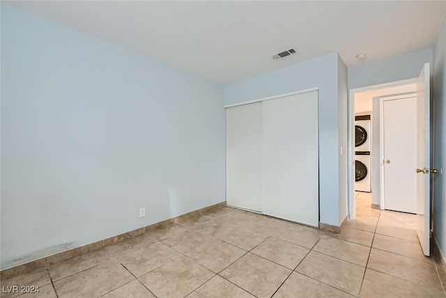 unfurnished bedroom with light tile patterned floors, stacked washer and clothes dryer, and a closet