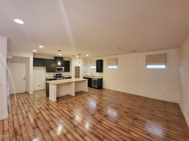 kitchen featuring light wood-type flooring, a center island, stainless steel appliances, sink, and decorative light fixtures