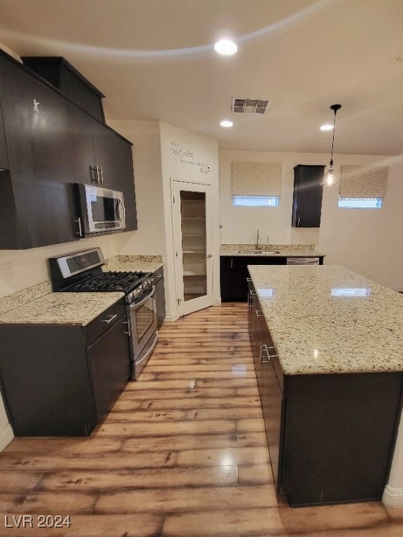 kitchen featuring a kitchen island, light hardwood / wood-style flooring, stainless steel appliances, light stone countertops, and pendant lighting