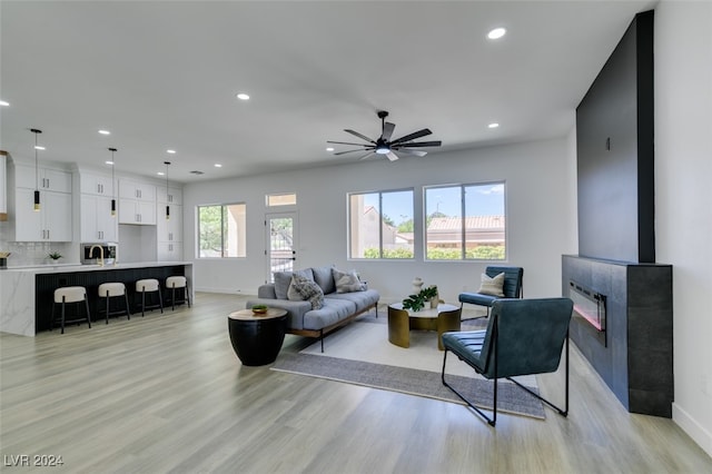 living room featuring light hardwood / wood-style floors, ceiling fan, and a tiled fireplace