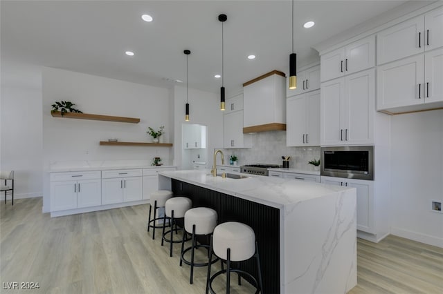 kitchen featuring white cabinetry, sink, hanging light fixtures, light stone counters, and a kitchen island with sink