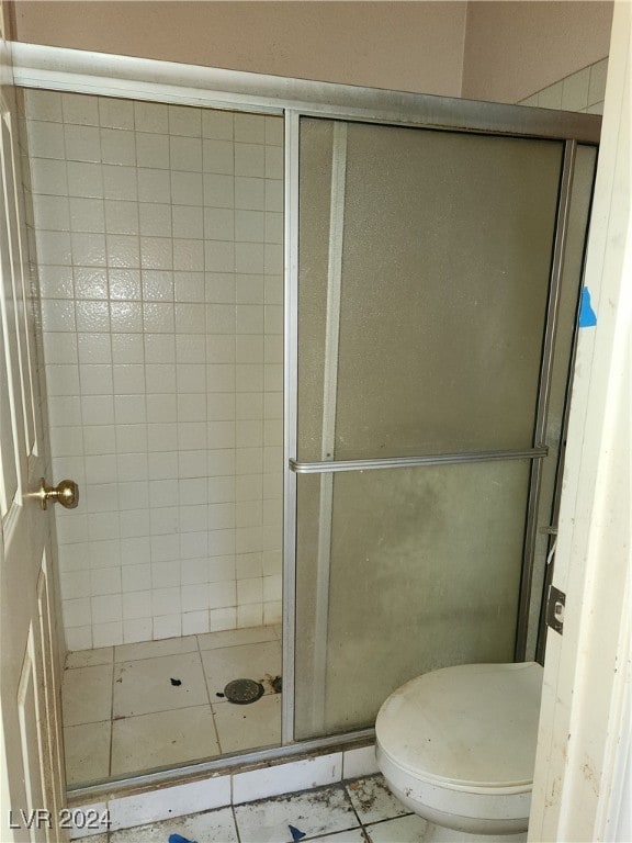 bathroom featuring tile patterned floors, a shower with shower door, and toilet