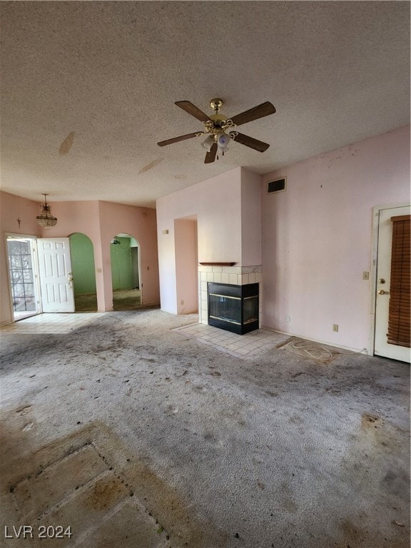 unfurnished living room with a tiled fireplace, ceiling fan, a textured ceiling, and carpet floors