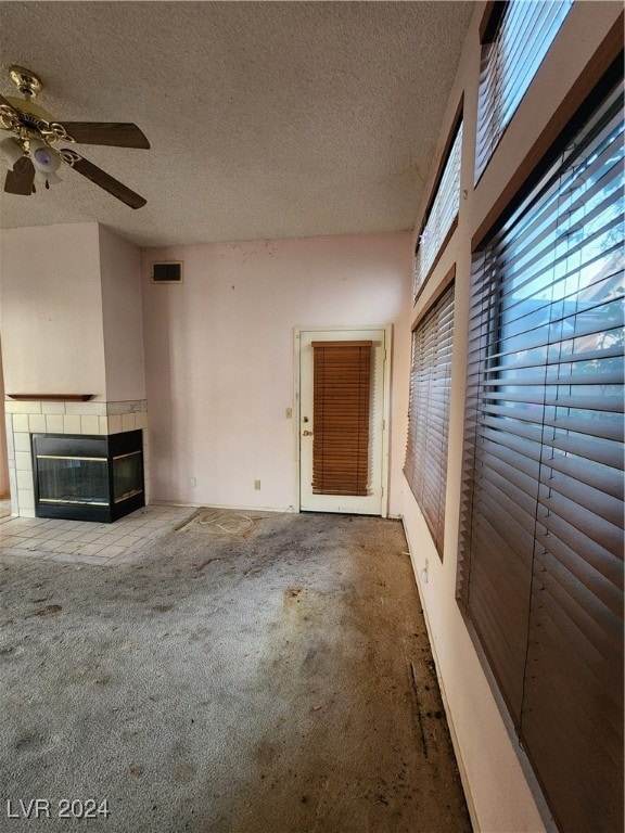 unfurnished living room with ceiling fan, a textured ceiling, carpet floors, and a fireplace