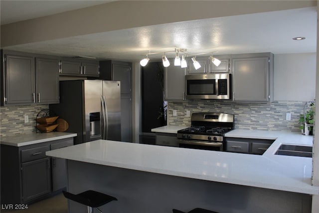 kitchen featuring gray cabinetry, stainless steel appliances, a breakfast bar area, and kitchen peninsula