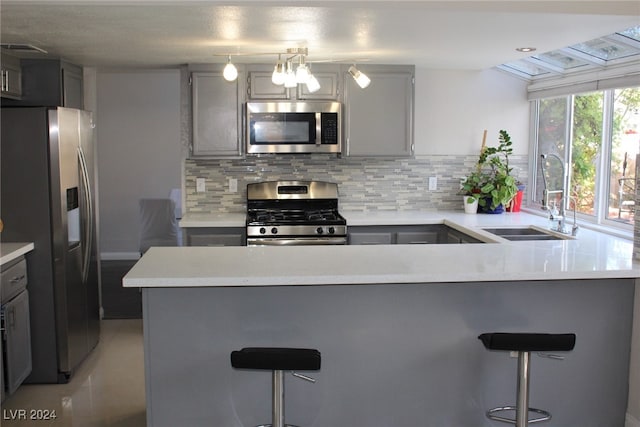 kitchen with gray cabinets, sink, appliances with stainless steel finishes, and a kitchen bar