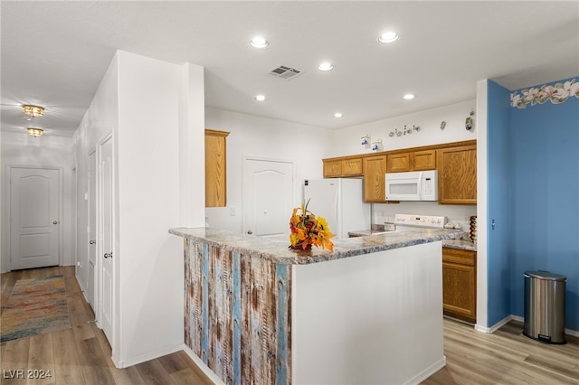 kitchen with light stone countertops, light hardwood / wood-style floors, kitchen peninsula, and white appliances