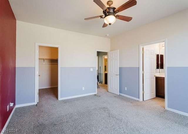 unfurnished bedroom featuring a closet, a walk in closet, ceiling fan, connected bathroom, and light carpet