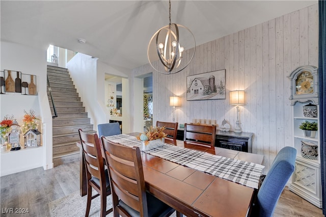 dining room with wood walls, a notable chandelier, and light hardwood / wood-style floors