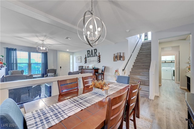 dining space featuring washing machine and clothes dryer, a notable chandelier, and light wood-type flooring