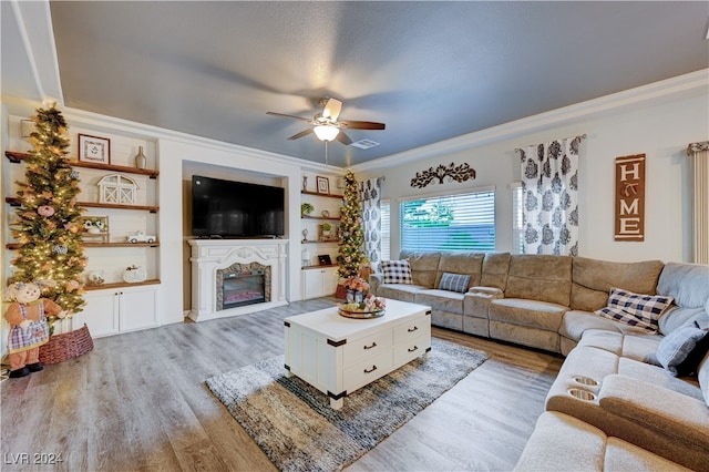 living room featuring built in features, light hardwood / wood-style flooring, ceiling fan, and crown molding