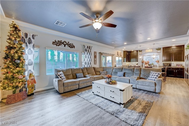 living room with a textured ceiling, light wood-type flooring, ceiling fan, and ornamental molding