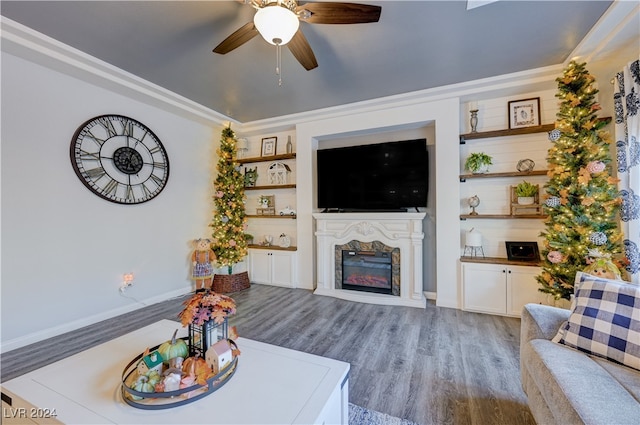 living room with built in shelves, ceiling fan, wood-type flooring, and ornamental molding