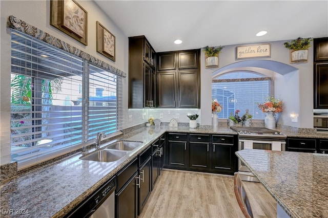 kitchen with sink, tasteful backsplash, light stone counters, stainless steel range oven, and light wood-type flooring