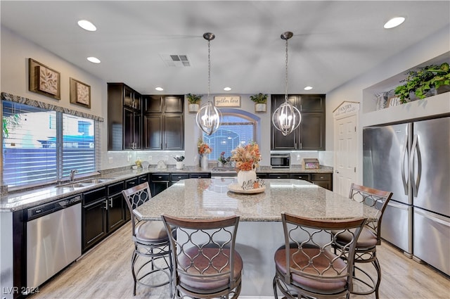 kitchen featuring dark brown cabinetry, hanging light fixtures, light hardwood / wood-style flooring, a kitchen island, and appliances with stainless steel finishes