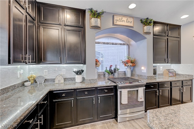 kitchen featuring stainless steel electric range, backsplash, light stone countertops, light hardwood / wood-style floors, and dark brown cabinetry