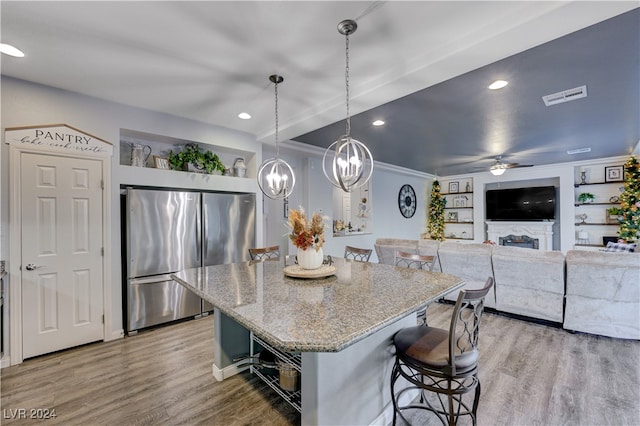 kitchen with light stone countertops, hanging light fixtures, stainless steel fridge, light hardwood / wood-style floors, and a kitchen island