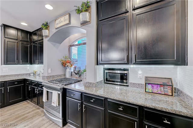 kitchen featuring tasteful backsplash, light stone countertops, appliances with stainless steel finishes, and light hardwood / wood-style flooring