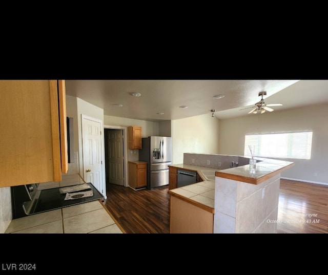 kitchen featuring tile counters, dark hardwood / wood-style floors, stainless steel refrigerator with ice dispenser, dishwashing machine, and a center island with sink