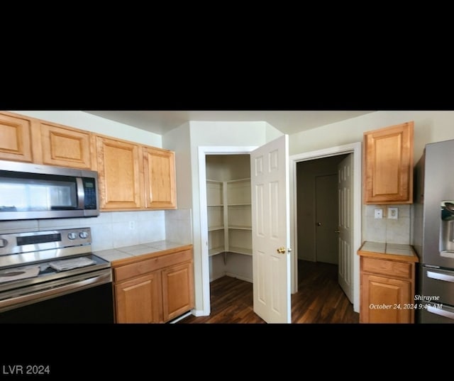 kitchen with dark wood-type flooring, appliances with stainless steel finishes, decorative backsplash, and tile counters