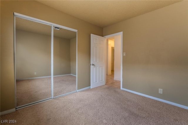 unfurnished bedroom featuring a textured ceiling, light colored carpet, and a closet