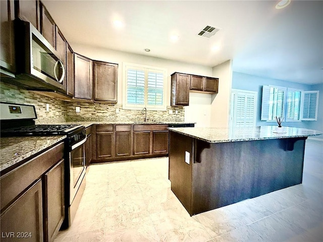 kitchen featuring light stone countertops, sink, stove, a breakfast bar area, and dark brown cabinets