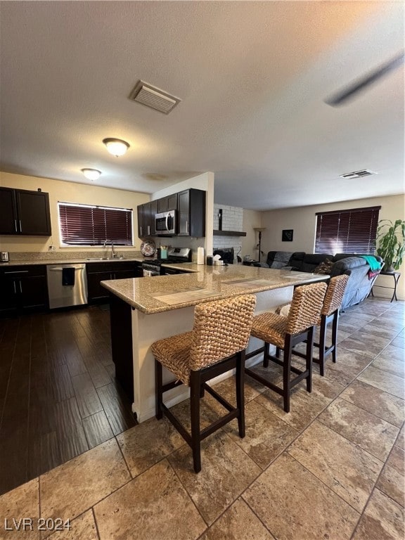 kitchen featuring light stone countertops, a textured ceiling, stainless steel appliances, sink, and a breakfast bar area