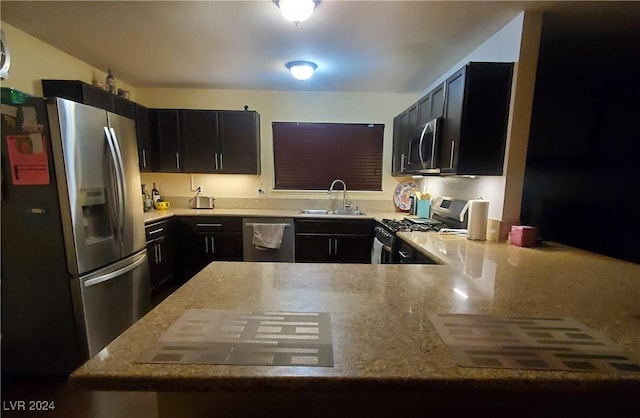 kitchen with light stone countertops, kitchen peninsula, appliances with stainless steel finishes, and sink