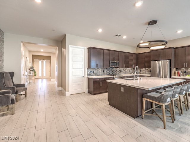 kitchen featuring a kitchen island with sink, backsplash, appliances with stainless steel finishes, dark brown cabinets, and sink