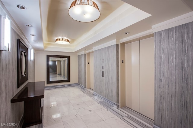 hall with wood walls and a tray ceiling