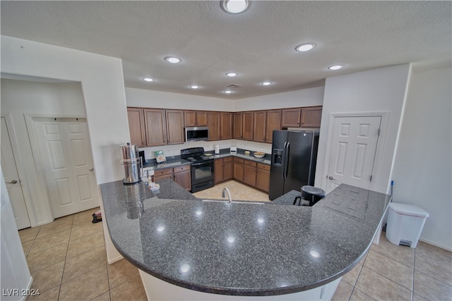 kitchen with light tile patterned flooring, a textured ceiling, and black appliances