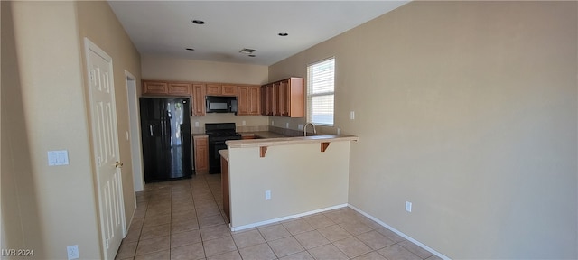 kitchen with kitchen peninsula, black appliances, a kitchen bar, and light tile patterned floors